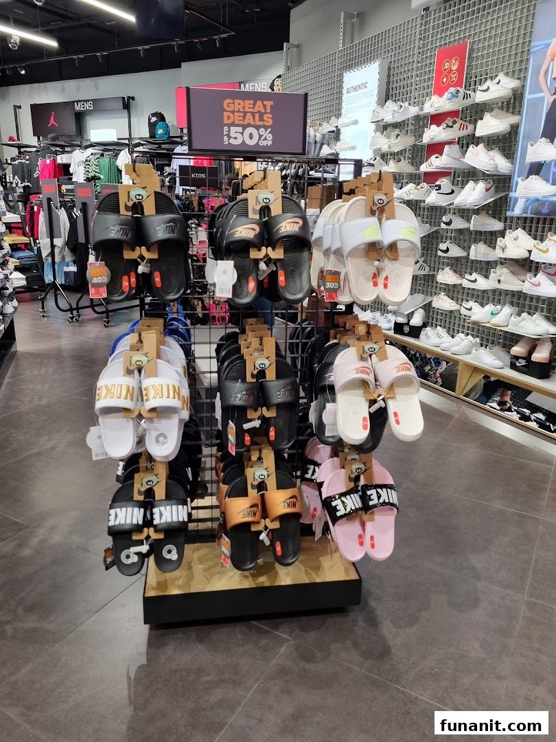 An interior view of JD Sports showcasing a display of Nike sandals and a wall of sneakers, with a 'Great Deals' sign.
