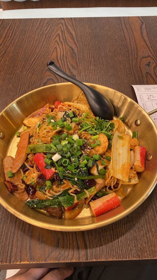 A vibrant, savory noodle dish with various ingredients served in a golden pan on a wooden table.