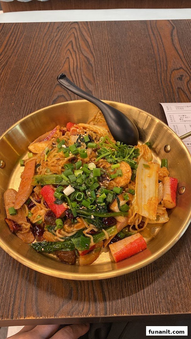 A vibrant, savory noodle dish with various ingredients served in a golden pan on a wooden table.