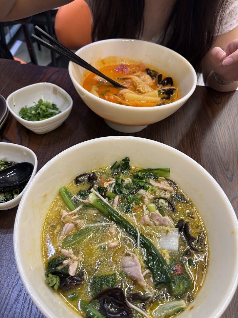 Two vibrant bowls of Asian-style soup or noodles with fresh ingredients on a wooden table.