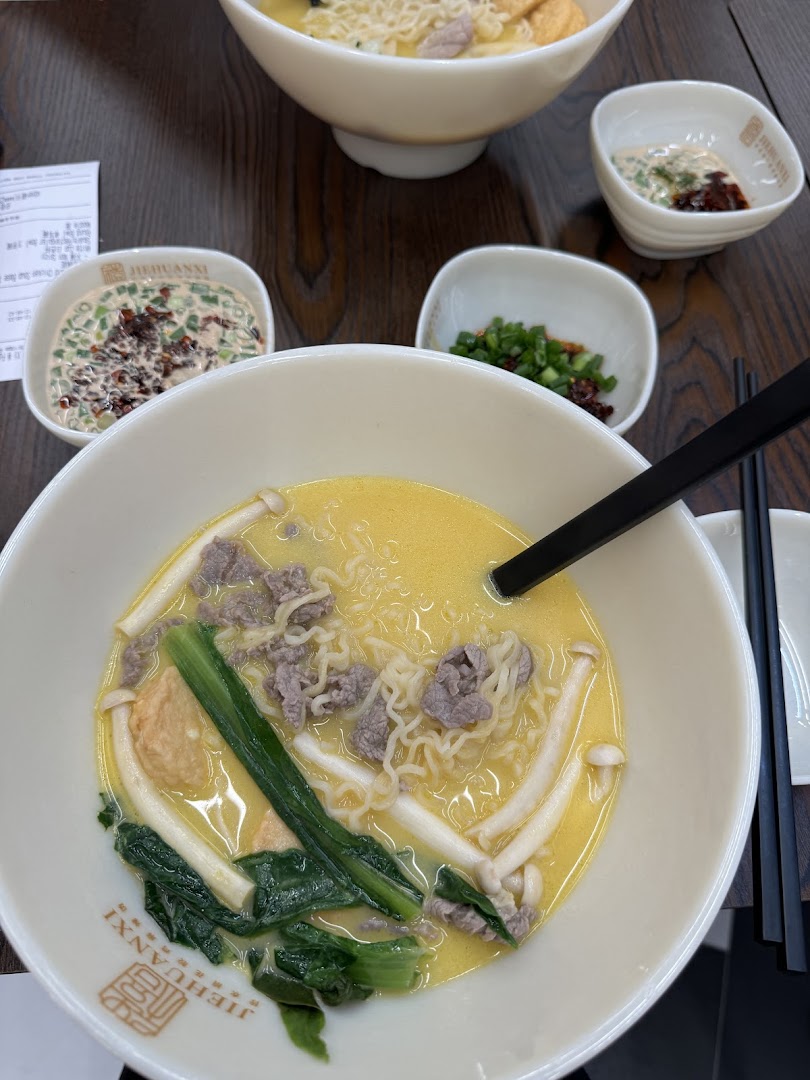 A close-up of a delicious bowl of noodles with beef, mushrooms, and greens, served with side condiments.
