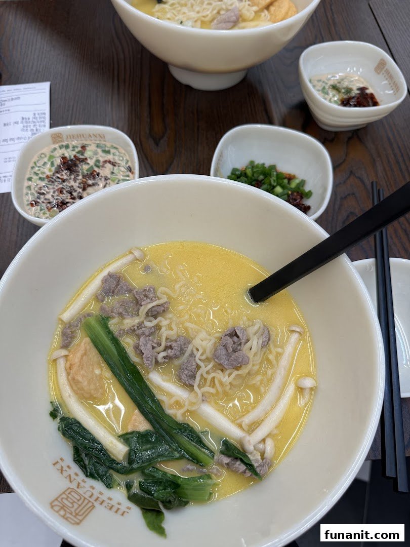 A close-up of a delicious bowl of noodles with beef, mushrooms, and greens, served with side condiments.