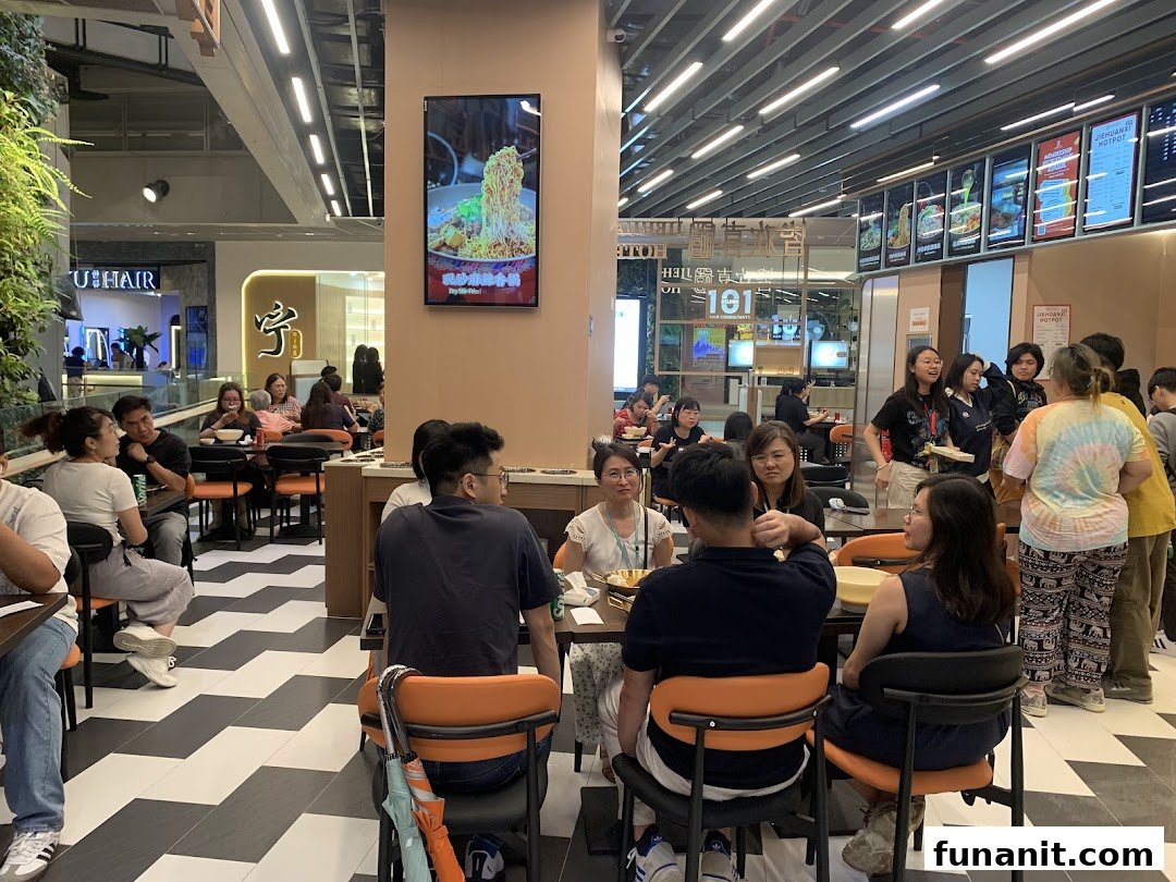 Customers dine and wait in a bustling, modern food court or restaurant setting with a digital menu display.
