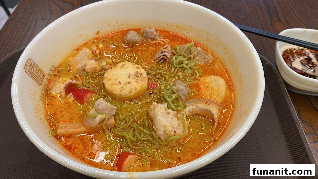 A vibrant bowl of spicy noodles with various toppings and green noodles from Jie Huan Xi.