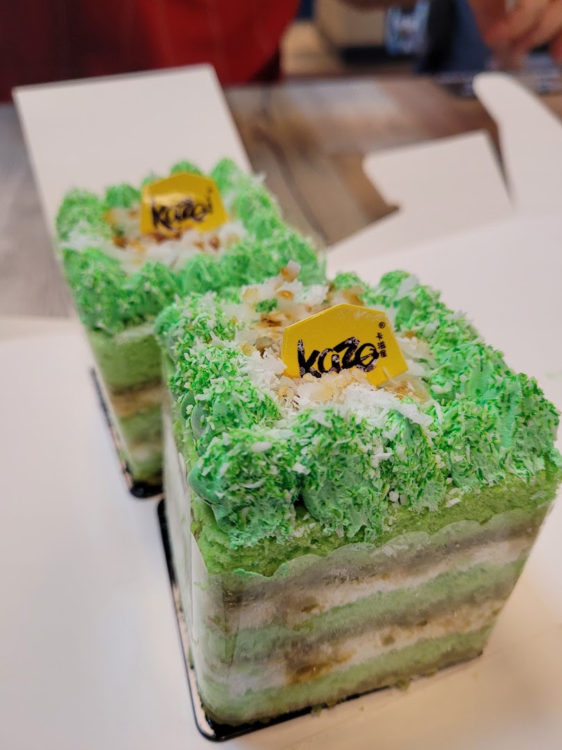 Two vibrant green layered cakes with Kazo branding, topped with coconut flakes, in white boxes.