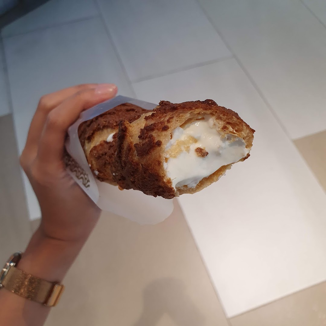 A hand holds a delicious cream puff filled with white cream, showcasing its crispy texture.