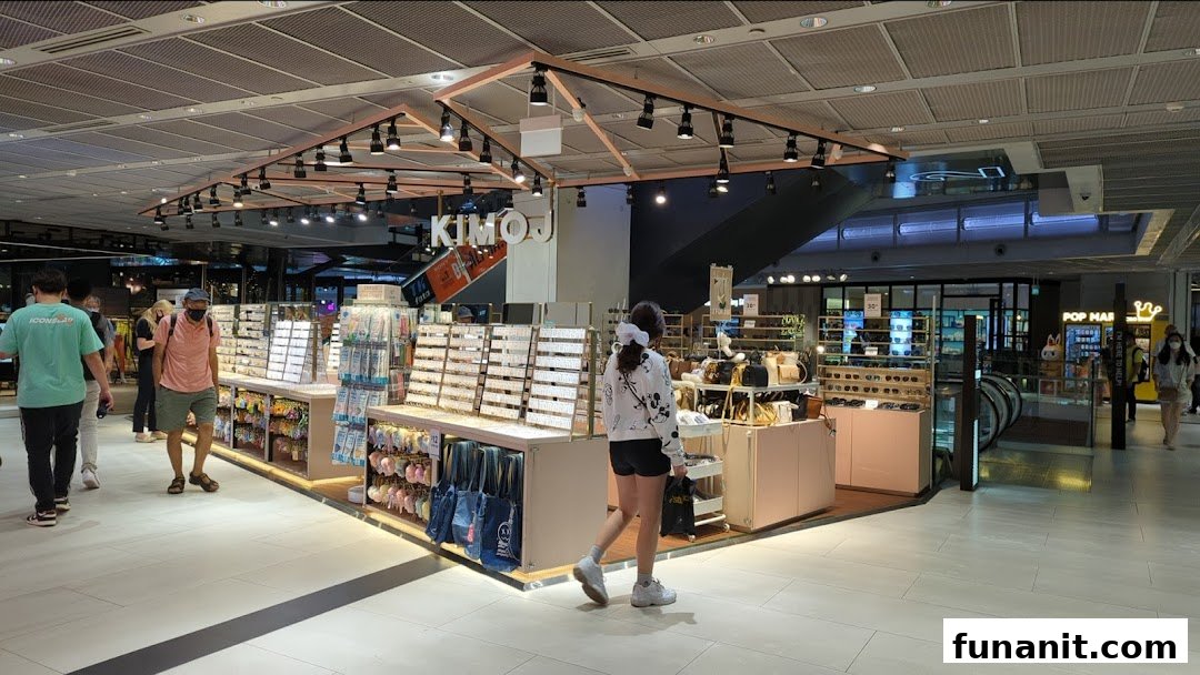 KIMOJ retail kiosk in a mall, showcasing accessories, sunglasses, and bags, with shoppers browsing.