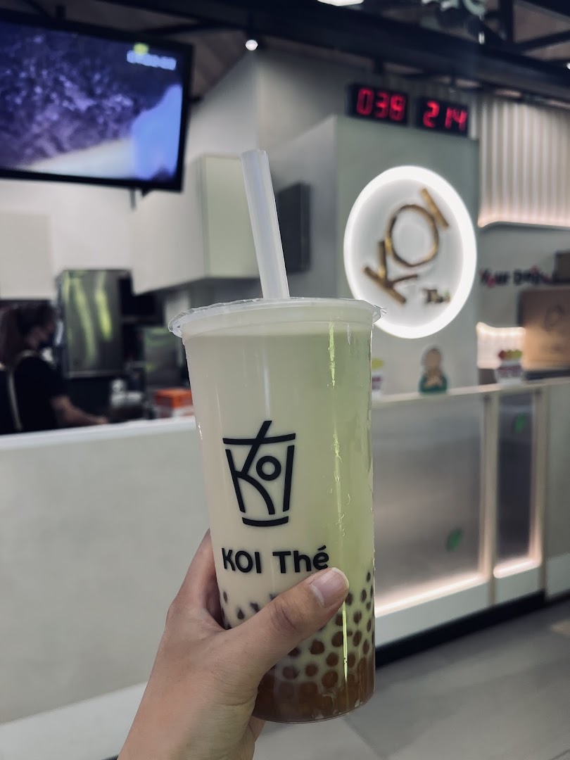 A hand holds a refreshing KOI Thé bubble tea cup inside the shop.