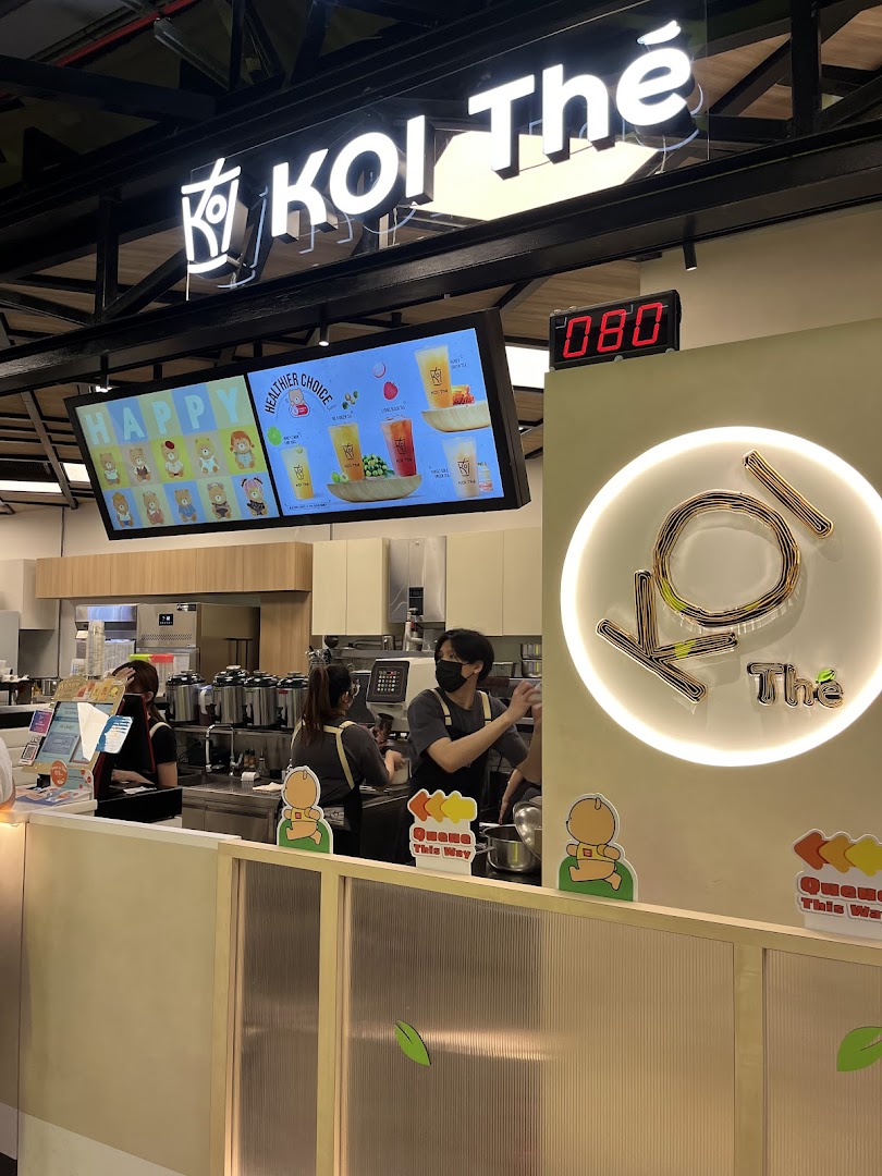 Interior view of KOI Thé Funan, showing staff preparing drinks behind the counter and digital menu displays.