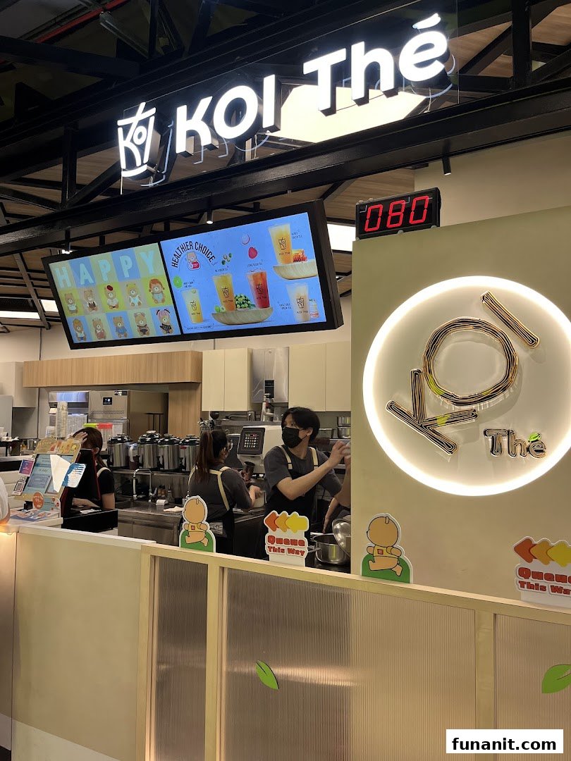 Interior view of KOI Thé Funan, showing staff preparing drinks behind the counter and digital menu displays.