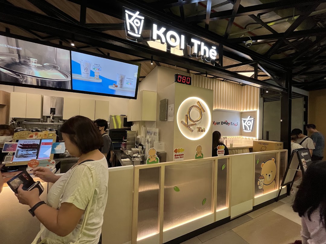 Customers at the KOI Thé counter, with digital displays showing beverages and branding.