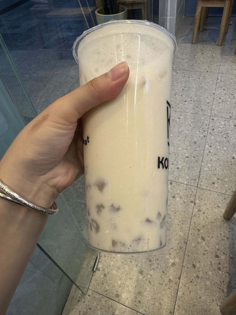 A hand holding a large bubble tea drink with taro bits from KOI Thé.