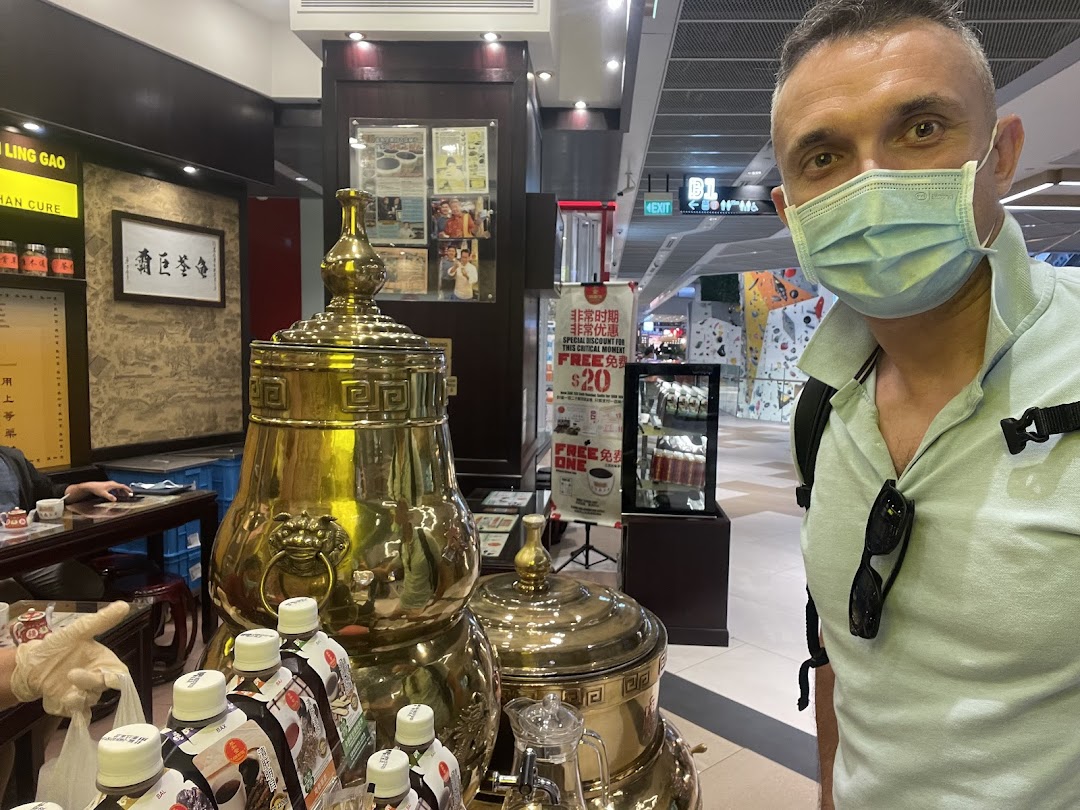 Interior view of Koong Woh Tong featuring traditional golden urns, bottled products, and a customer.