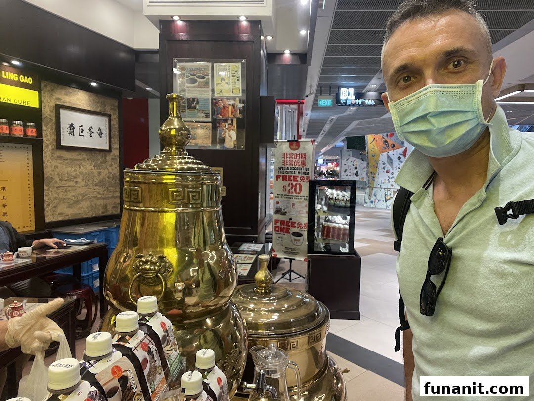 Interior view of Koong Woh Tong featuring traditional golden urns, bottled products, and a customer.