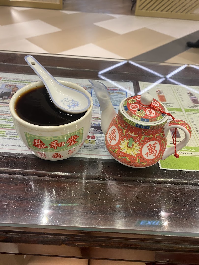 A traditional herbal jelly or tea in a cup with a spoon, alongside a decorative teapot on a wooden table.