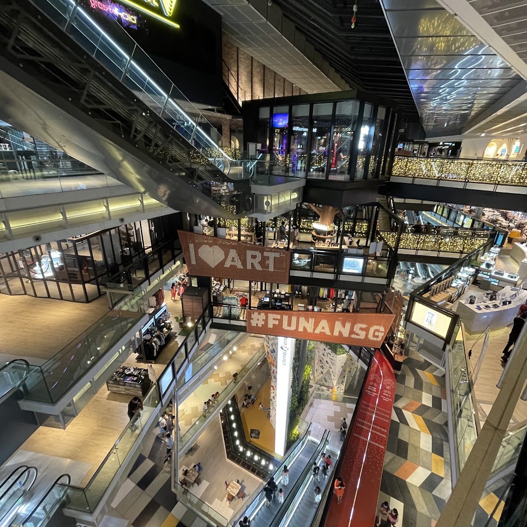 An expansive view of Funan Mall's multi-level interior, featuring escalators, shops, and a prominent climbing wall.