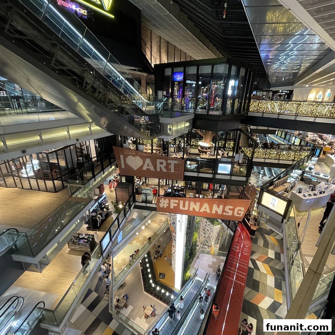 An expansive view of Funan Mall's multi-level interior, featuring escalators, shops, and a prominent climbing wall.