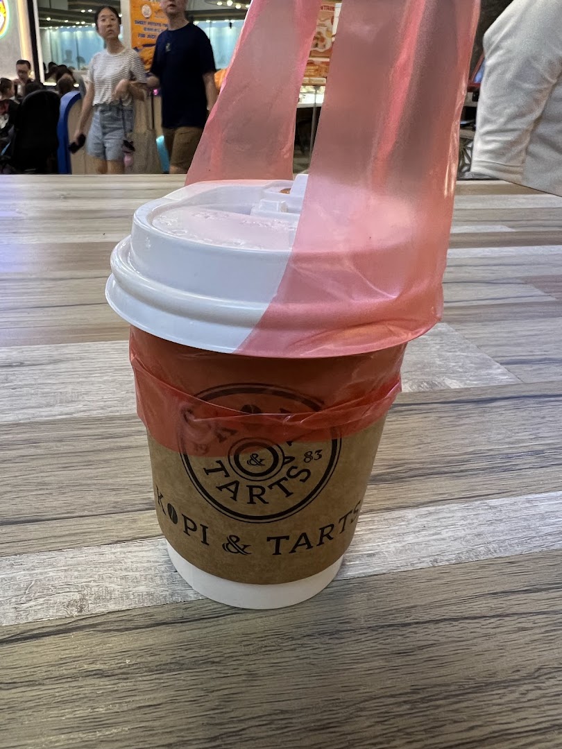 A Kopi & Tarts takeaway cup with a red plastic carrier sits on a wooden table.
