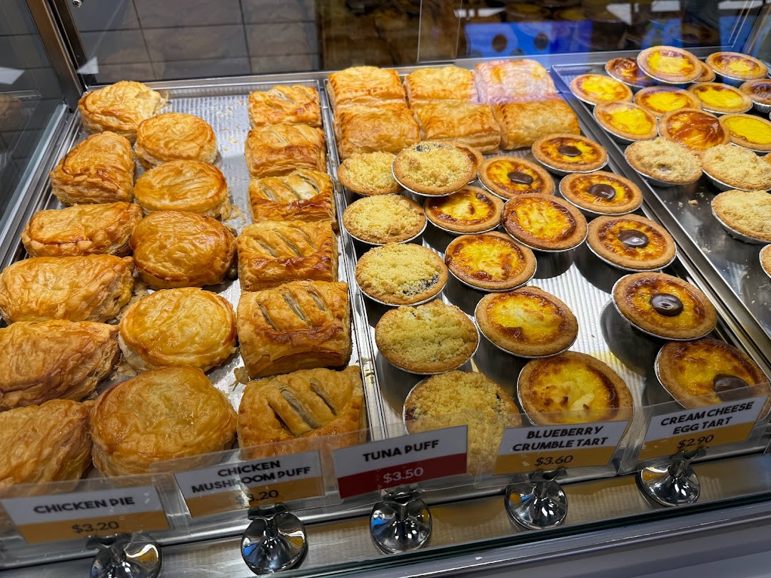 A vibrant display of freshly baked savory pastries and sweet tarts with visible price tags.