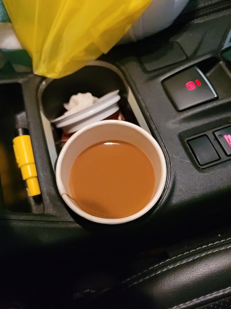 A cup of coffee or tea from Kopi Tarts in a car's cup holder, ready for a commute.