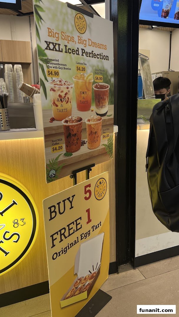 A promotional stand showcasing iced drinks and an egg tart offer from Kopi Tarts.