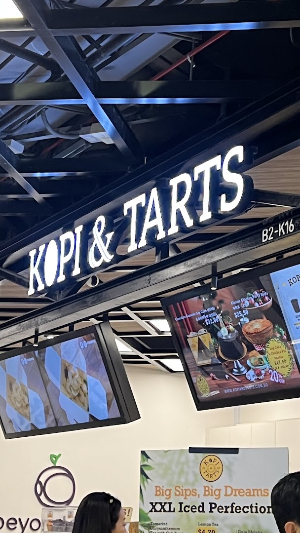 An illuminated Kopi & Tarts sign above digital screens displaying various food and drink offerings.
