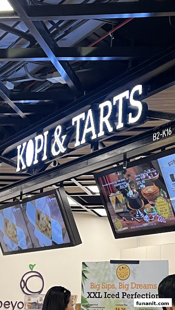An illuminated Kopi & Tarts sign above digital screens displaying various food and drink offerings.