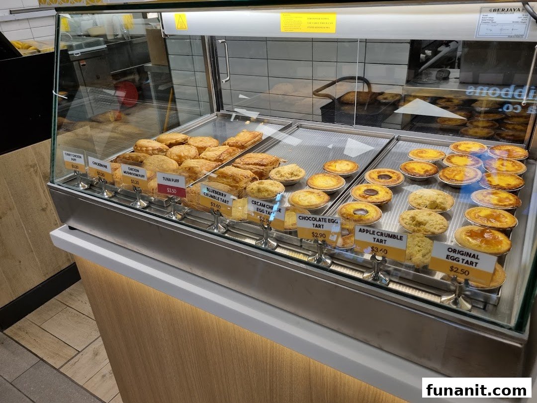 A vibrant display case showcasing a variety of freshly baked tarts and savory puffs with clear price tags.