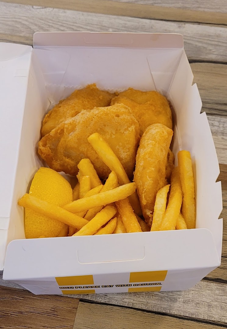 A takeaway box filled with golden-fried fish or chicken pieces, crispy french fries, and a lemon wedge.