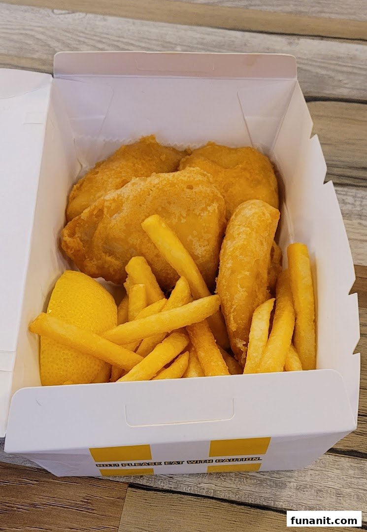 A takeaway box filled with golden-fried fish or chicken pieces, crispy french fries, and a lemon wedge.