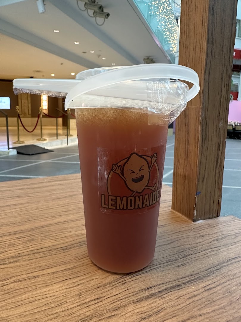 A refreshing Lemonaide drink in a branded cup on a wooden surface.