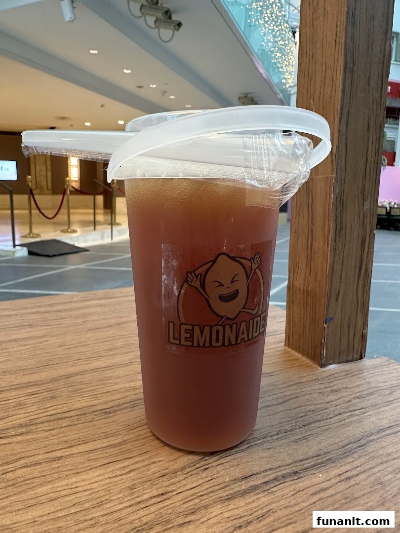 A refreshing Lemonaide drink in a branded cup on a wooden surface.