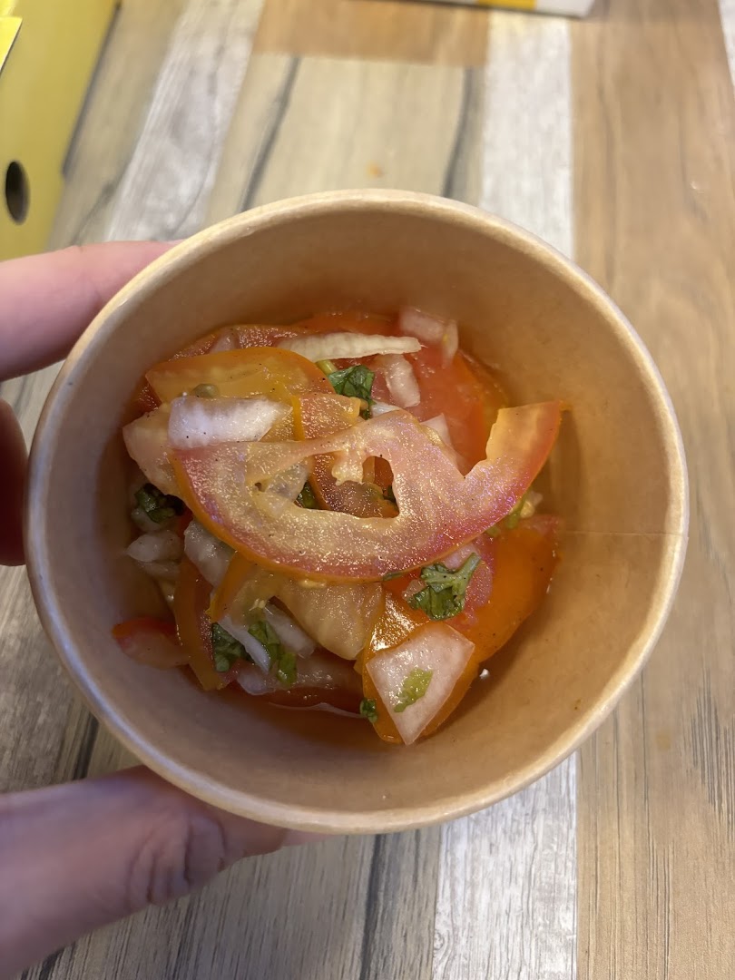 A close-up of a fresh tomato and onion salad with herbs in a paper cup.