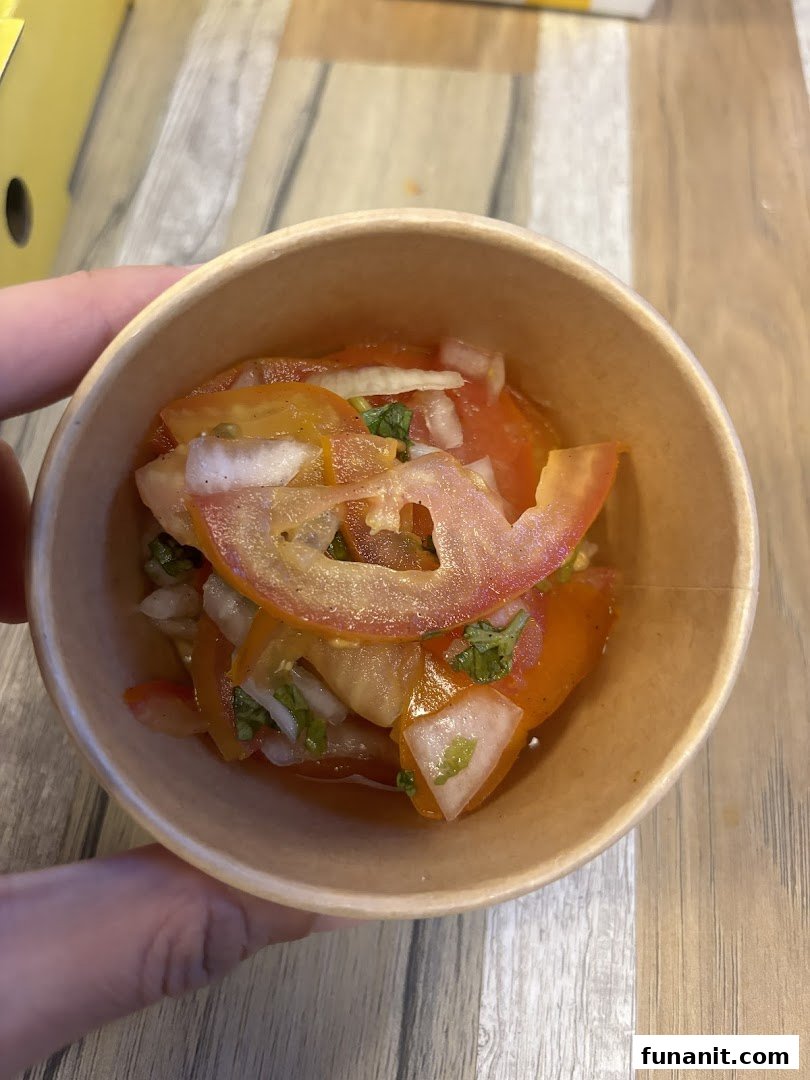 A close-up of a fresh tomato and onion salad with herbs in a paper cup.