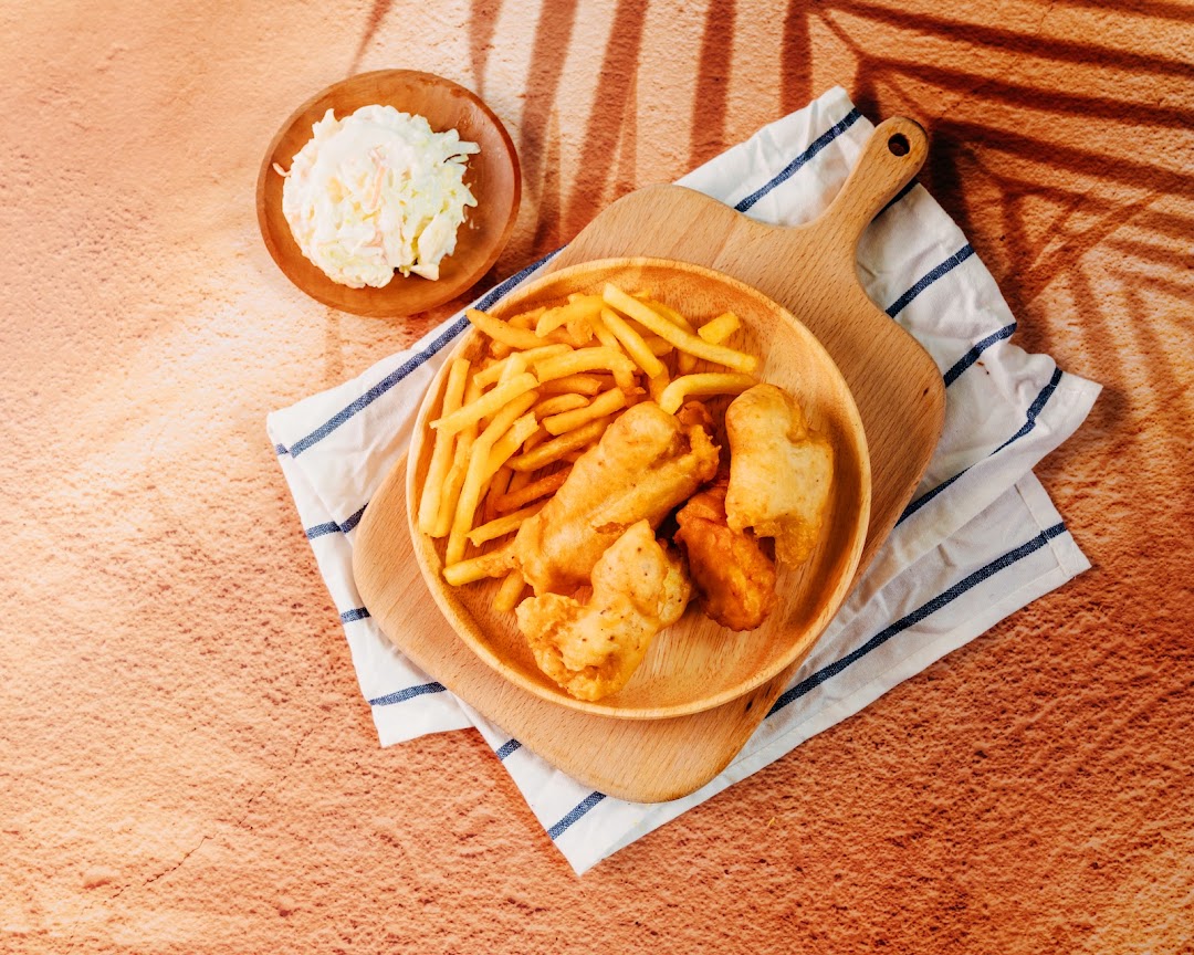 A wooden plate of golden fish and chips with a side of coleslaw on a textured surface.