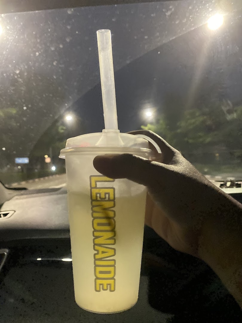 A hand holds a refreshing cup of Lemonaide with a straw, illuminated at night.
