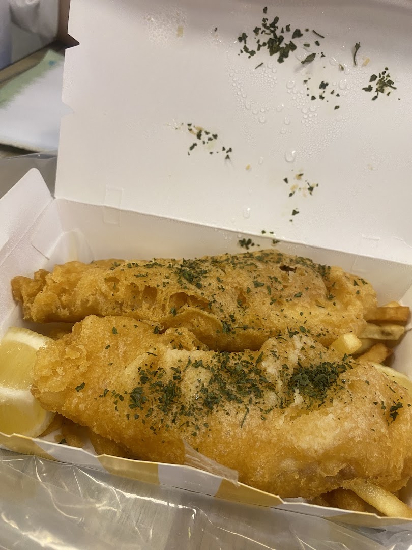 Two pieces of golden-fried fish and chips with a lemon wedge in a takeout box.
