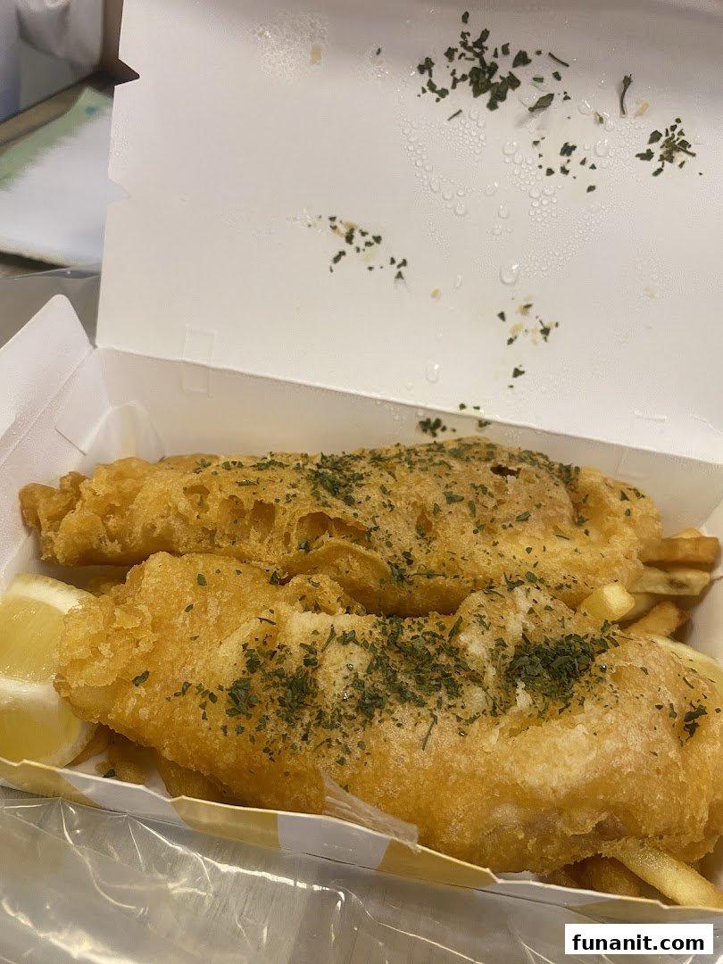 Two pieces of golden-fried fish and chips with a lemon wedge in a takeout box.