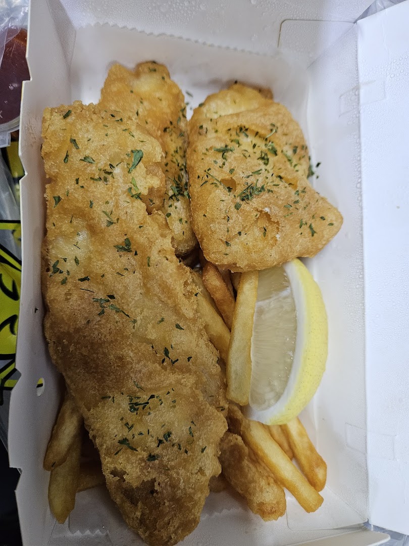 Golden fried fish and chips with a lemon wedge, garnished with parsley, in a takeout box.