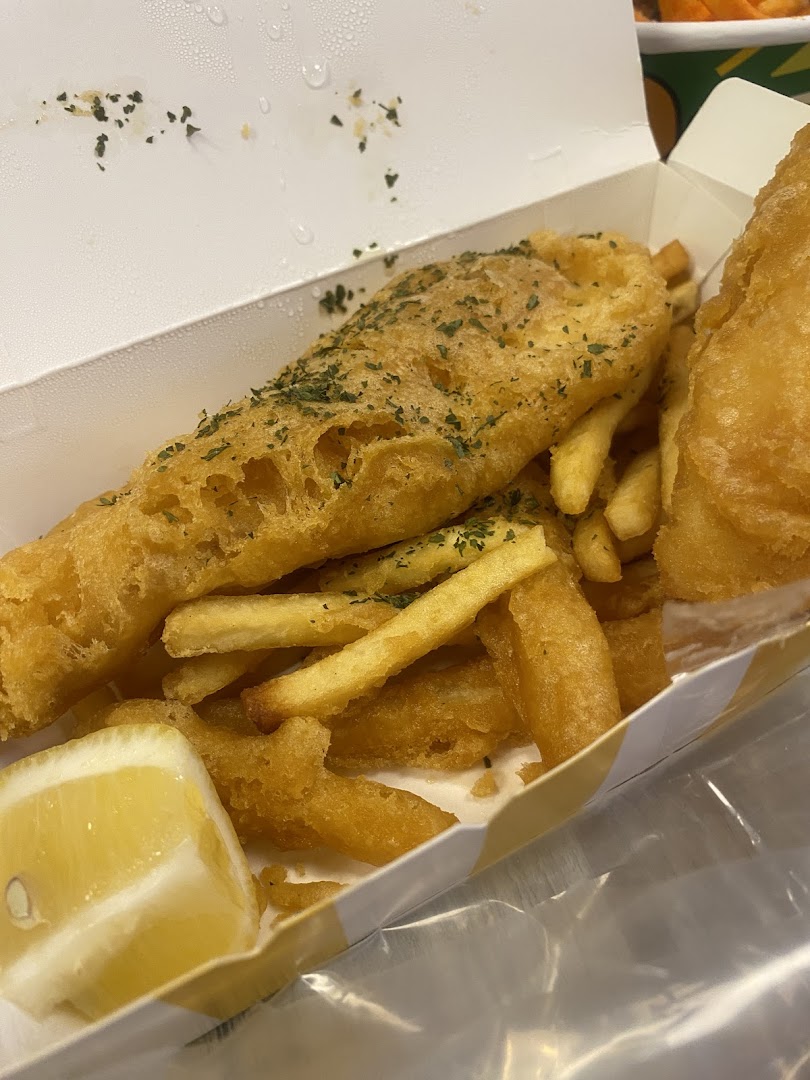 Golden fried fish and chips with a lemon wedge in a takeaway box.