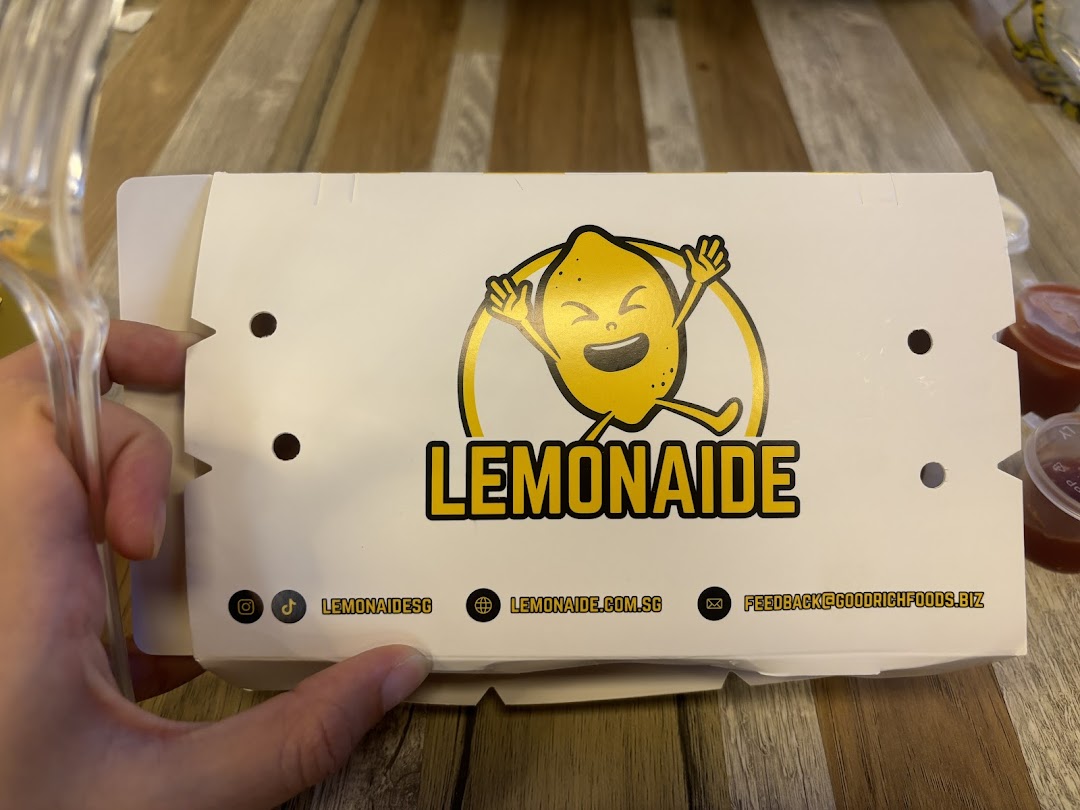 A white food box from Lemonaide featuring its cheerful lemon logo and contact details.