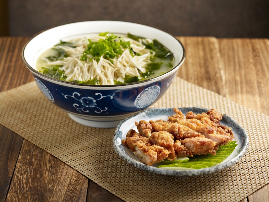 A comforting bowl of noodles with seaweed and a plate of crispy fried chicken on a wooden table.