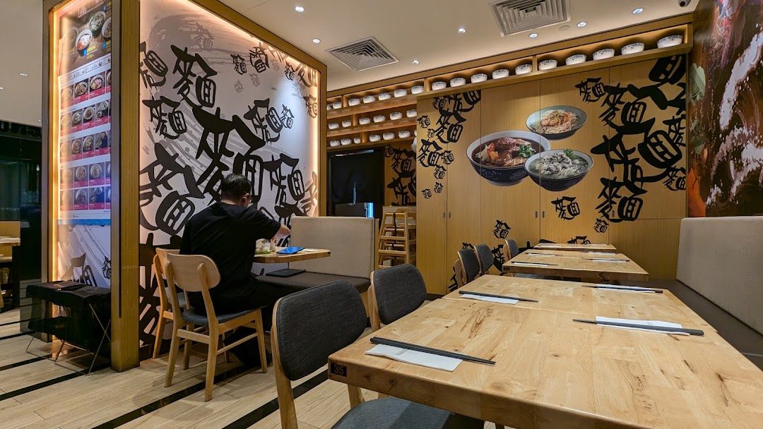 Interior view of LeNu Chefs Wai Noodle Bar, featuring wooden tables, comfortable seating, and a customer.