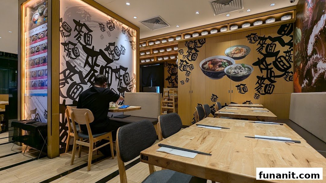 Interior view of LeNu Chefs Wai Noodle Bar, featuring wooden tables, comfortable seating, and a customer.