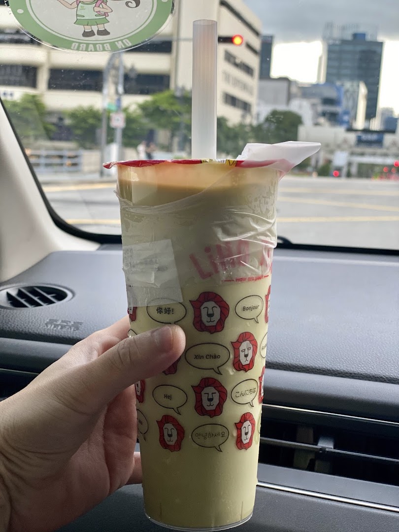 A hand holds a LiHO TEA beverage cup with a city background visible through a car window.