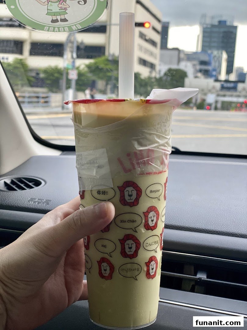 A hand holds a LiHO TEA beverage cup with a city background visible through a car window.