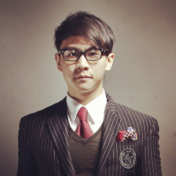 A stylishly dressed man in a pinstripe suit, white shirt, red tie, and glasses.