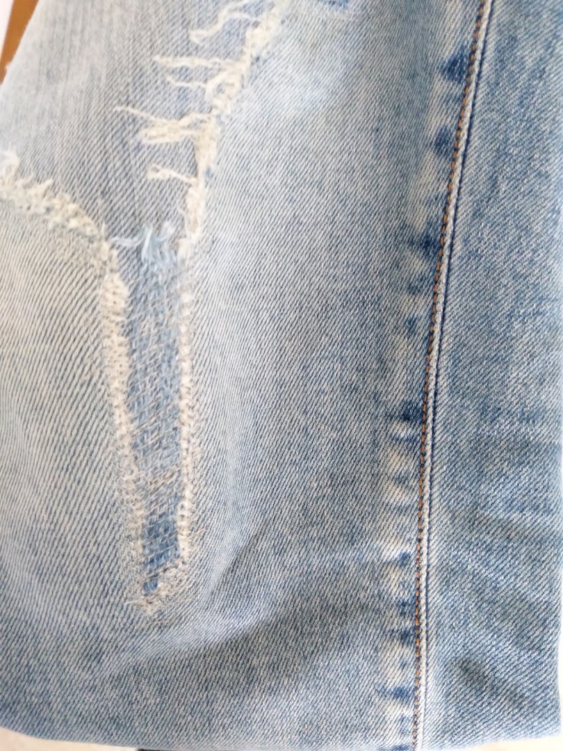 Close-up of light blue distressed denim fabric, showcasing repair or alteration details with visible stitching.