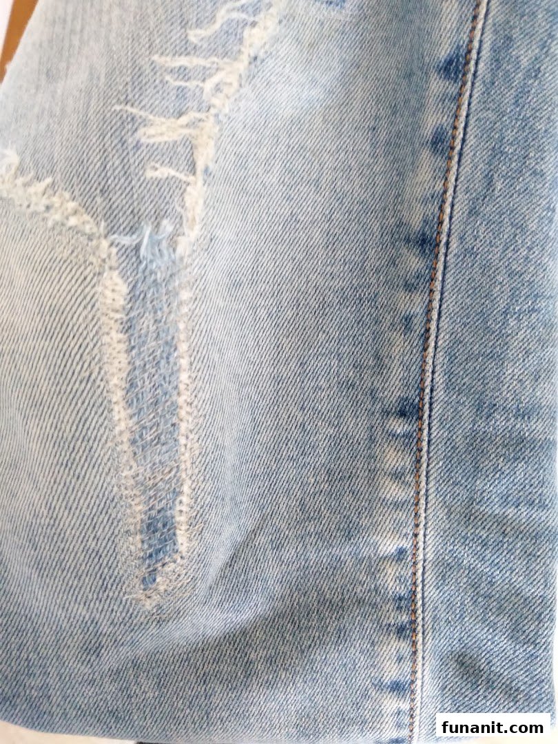 Close-up of light blue distressed denim fabric, showcasing repair or alteration details with visible stitching.