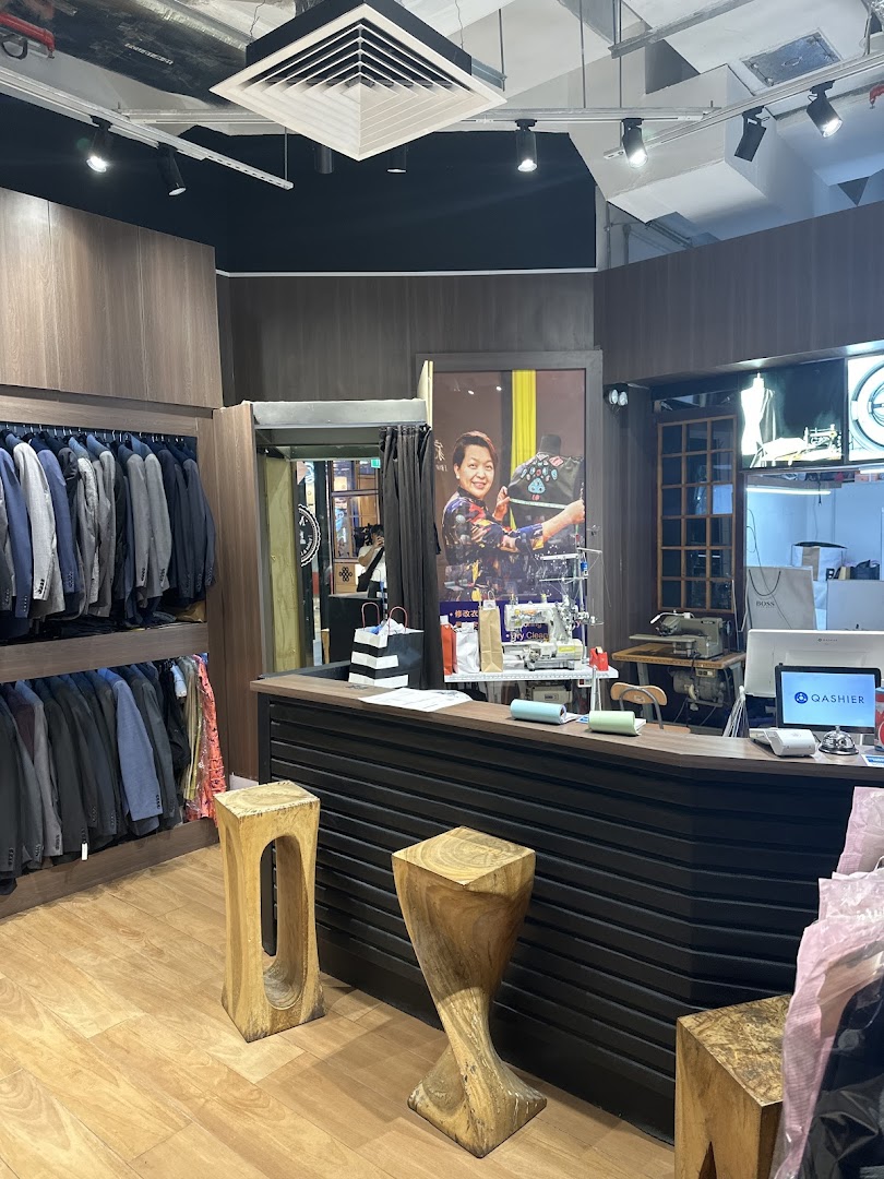 Interior view of May Tailor Laundry, featuring clothing racks, a service counter, and a large promotional poster.